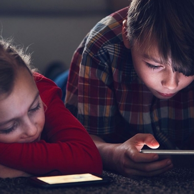 A young girl lying on the floor watching something on a smart phone while a boy beside her looks at something on a electronic tablet. (Photo: Getty Images)