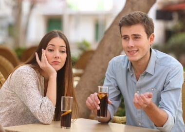 Caucasin couple sitting at a table outside drinking cola. He is talking and she looks bored. (Photo: Shutterstock)