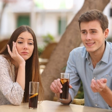 Caucasin couple sitting at a table outside drinking cola. He is talking and she looks bored. (Photo: Shutterstock)