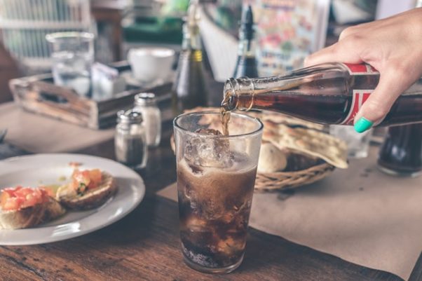 A hand pouring Coke from a bottle into a glass with ice. (Photo: Artem Beliaikin/Pexels)