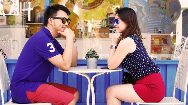 Asian couple sitting across the table from each other at an outdoor cafe. (Photo: Pexels)