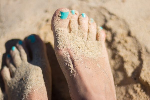 Woman's feet in the sand with her toenails painted a shade of aqua. (Photo: Juja Han/Unsplash)