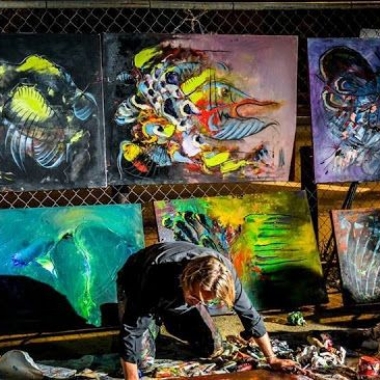 A man paining a picture with several pictures diplayed behind him. (Photo: Art All Night)