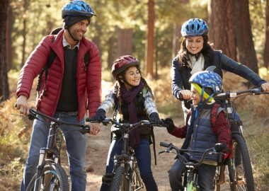 Two Hispanic parents with their son and daughter on bikes in a park on a path in the woods. (Photo: Getty Images)