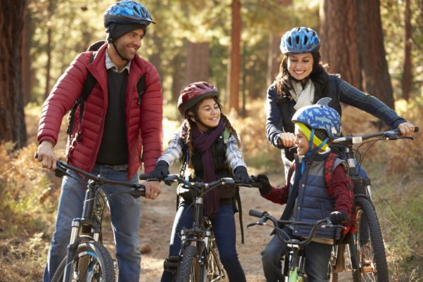 Two Hispanic parents with their son and daughter on bikes in a park on a path in the woods. (Photo: Getty Images)