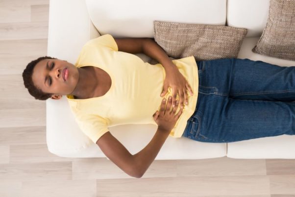 African American woman lying on her back holding her abdomen. (Photo: Shutterstock)