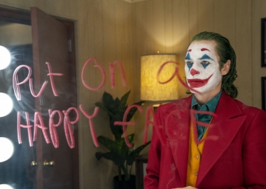 Arthur Fleck (Joaquin Phoenix) dressed as a clown stares into a mirror with 
