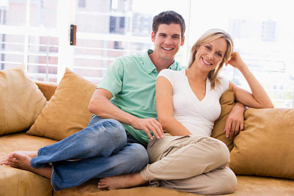 Younger man an dolder woman relaxing in living room smiling. (Photo: iStock)