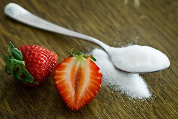 Close up of a halved strawberry with a spoonful of sugar. (Photo: Mali Maeder/Pexels)