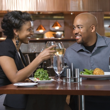 African-American couple dining out. They are toasting with glasses of white wine and smiling. (Photo: Bigstock)