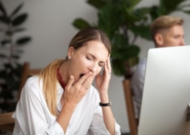 Woman sitting at her computer yawning as she covers her mouth. (Photo: Shutterstock)