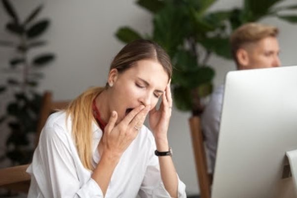 Woman sitting at her computer yawning as she covers her mouth. (Photo: Shutterstock)
