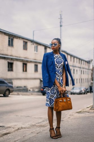 Woman in blue and white dress with blue jacket holding a brown purse outside. (Photo: godisable Jacob/Pexels)