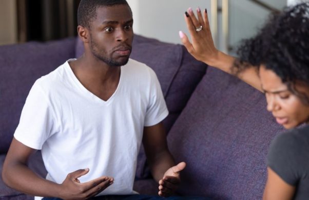 Black man on a couch pleading with a black woman who has her hand up in a stop signal. (Photo: Shutterstock)