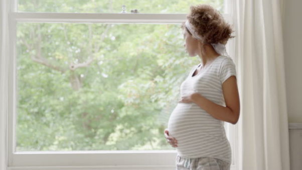 Pregnant woman looking out window at trees rubbing stomach. (Photo: iStock)