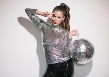 A woman dressed in a silver top holding a disco ball with her fingers in a V over her right eye. (Photo: Shutterstock)