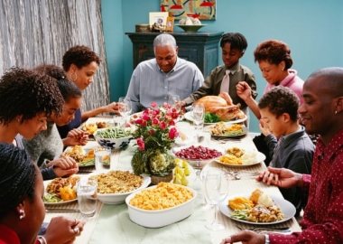 A black family holding hands and praying over a holiday meal with a whole turkey, mac and cheese, and other dishes. (Photo: Corbis)