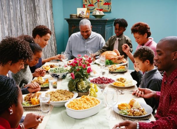 A black family holding hands and praying over a holiday meal with a whole turkey, mac and cheese, and other dishes. (Photo: Corbis)