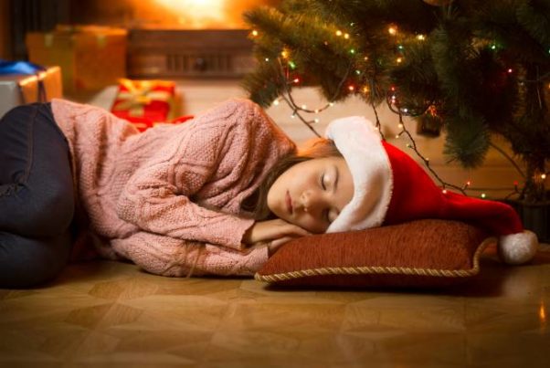 Woman alseep on the floor in front of the Christmas tree wearing a Santa cap. (Photo; 123rf)