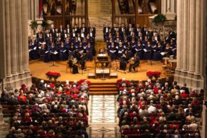 The National Cathedral Choral Society on stage in front of the audience with the sanctuary decorated with pointsettias. (Photo: National Cathedral)