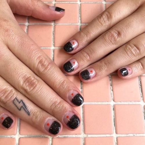 woman with the tips of her nails in black glitter and the bottoms clear with an orange dot in the middle. (Photo: Shorditch Nails & Academy/Instagram)