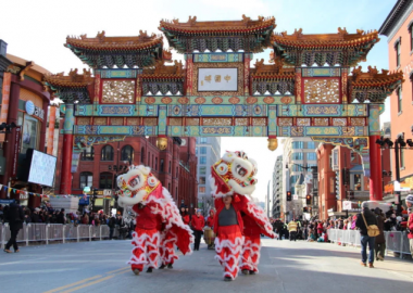 Two sets of dancers in lion cosumes walk under the Friendship Archway in Chinatown. (Photo: Edward Der)