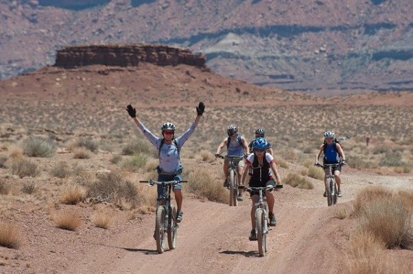 Five bicyclists in the dessert, one with both hands raised in the air. (Photo: skeeze/Pixabay)