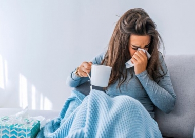 Woman in bed holding a cup of tea and blowing her nose. (Photo: Shutterstock)