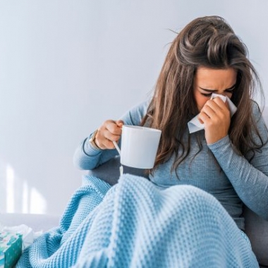 Woman in bed holding a cup of tea and blowing her nose. (Photo: Shutterstock)