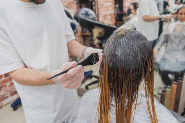 Male hairstylist applying color to a woman's hair in a beauty salon. (Photo: Maria Geller/Pexels)