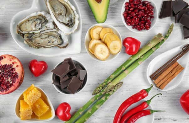 Several aphrodisiacs on a table including oysters, avocados, asparagus, bananas, chocolate and Thai chili peppers, some in heart-shaped bowls. (Photo: Shutterstock)