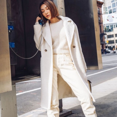 Asian woman wearing a white coat, sweater and pants talking on a payphone. (Photo: Jessica Wang)