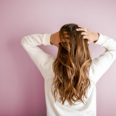 Woman with long hair in white long-sleeved shirt standing in front of pink wall. (Photo: Element5 Digital/Unsplash)