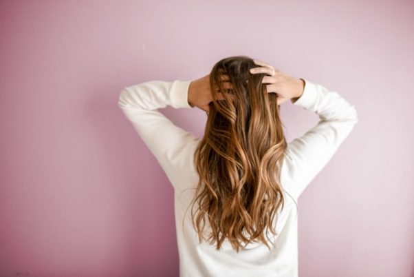 Woman with long hair in white long-sleeved shirt standing in front of pink wall. (Photo: Element5 Digital/Unsplash)
