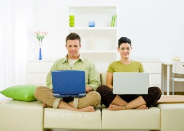 Man and woman working side-by-side on laptops while sitting on a white couch. (Photo: Shutterstock)