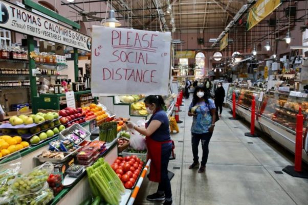 Shoppers at a produce stand in Eastern Market wearing masks while a sign hangs from the ceiling saying "Please Social Distance." (Photo: Evy Mages/Washingtonian)
