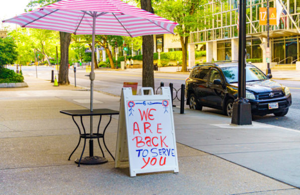 A table with umbrella in front of a restaurant with a sign that says "We are back to serve you." (Photo: Ted Eytan/Flickr)