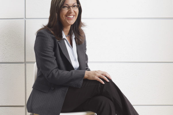 Hispanic businesswoman wearing a gray blazer, white shirt and dark gray pants sitting in waiting room. (Photo: Getty Images)