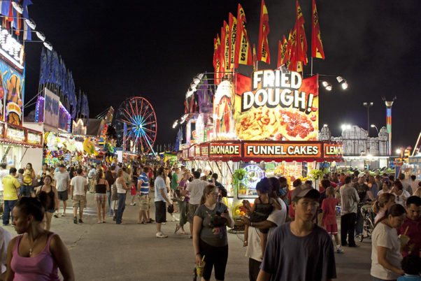 The midway at the Montgomery County Agriculrtural Fair lit up at night inclduign the farris wheel and a fried dough food stand. (Photo: Ryan Crierie/Flickr)