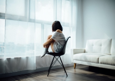 A woman sits on a chair in her living room looking out the window. (Photo: Anthony Tran/Unsplash)