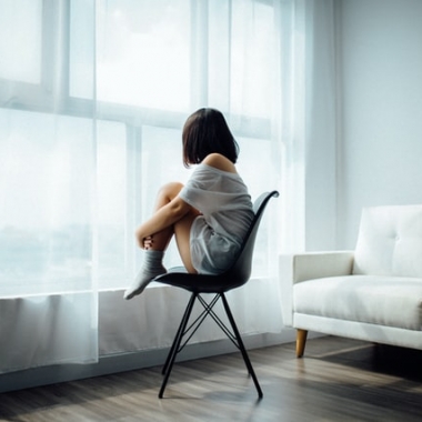 A woman sits on a chair in her living room looking out the window. (Photo: Anthony Tran/Unsplash)