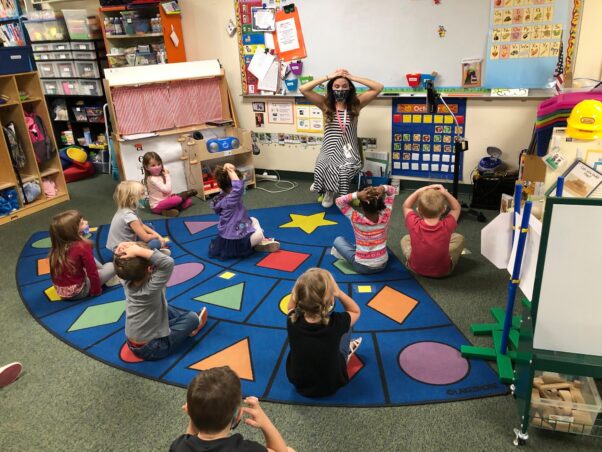 Young students sit on the floor in a classroom with their hands on their heads as they mimic their teacher. (Photo: Dorchester County Public Schools)