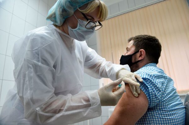 A man wearing a face covering gets a injection from a woman in full protective gear. (Photo: Natalia Kolesnikova/AFP/Getty Images)