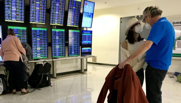 A couple wearing masks at BWI Airport stand near an arrival and departure board. (Photo: Baltimore Sun)