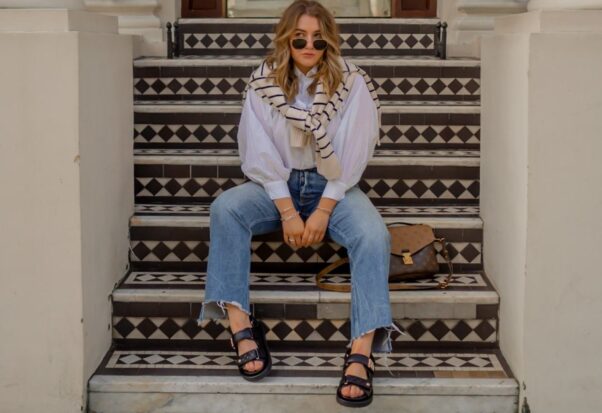 A woman sitting on outside steps in a white shirt, ripped jeans, Birkenstocks and sunglasses. (Photo: Elliee May)