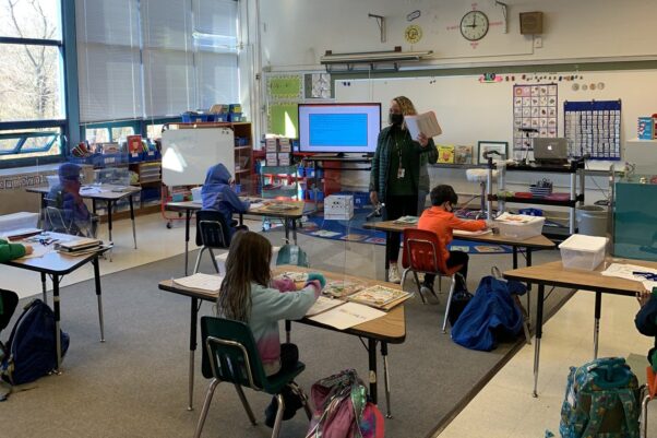 First grade students in a classroom at Jamestown Elemenatry Scool sit at their desks while their teacher reads a book. (Photo: Arlington Public Schools)
