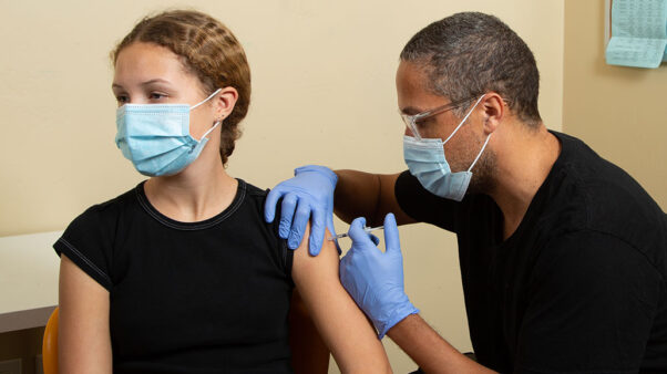A young woman getting a vaccine from a Black doctor. (Photo: Side Show Stock/iStock)