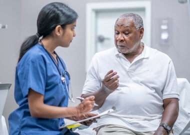 Black senior man talking to a female doctor in blue scrubs. (Photo; iStock)