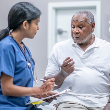 Black senior man talking to a female doctor in blue scrubs. (Photo; iStock)