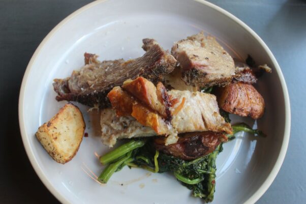 Porchetta roast with roasted red potatoes and spicy broccoli rabe on a white plate. (Photo: Mark Heckathorn/DC on Heels) 